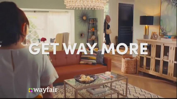 Wayfair电视节目广告。一位女士站在一间装饰过家具的房间里，上面写着:“得到更多”。