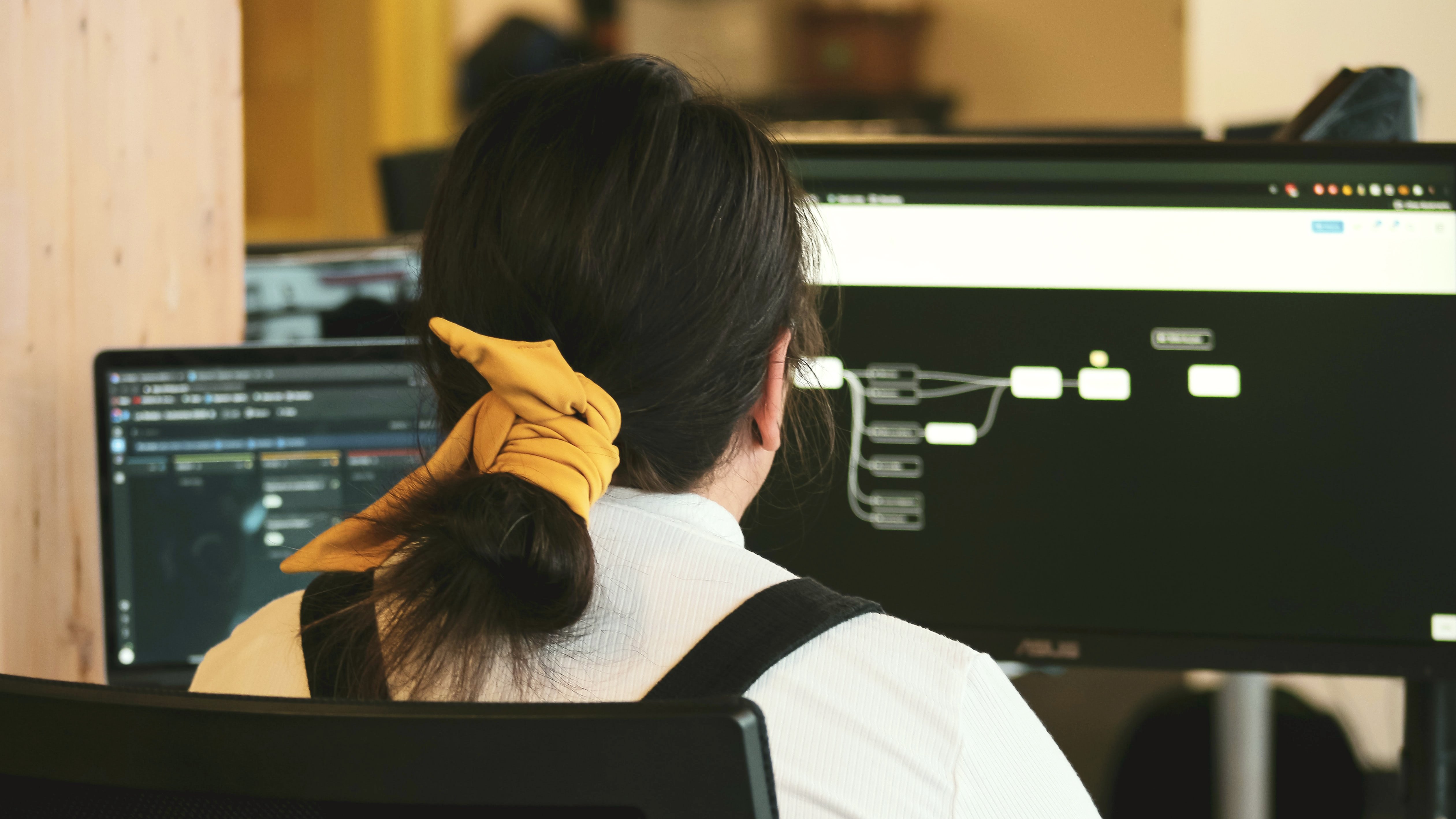 戴着黄色领带的女人面对着电脑屏幕，屏幕上显示着工作流程。